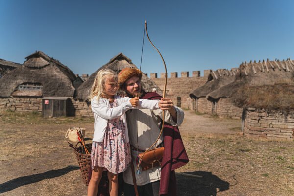 Ett barn skjuter pilbåge med hjälp av en guide i medeltida kläder,