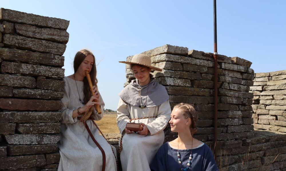 Tre kvinnor i medeltida kläder sitter på borgmuren.