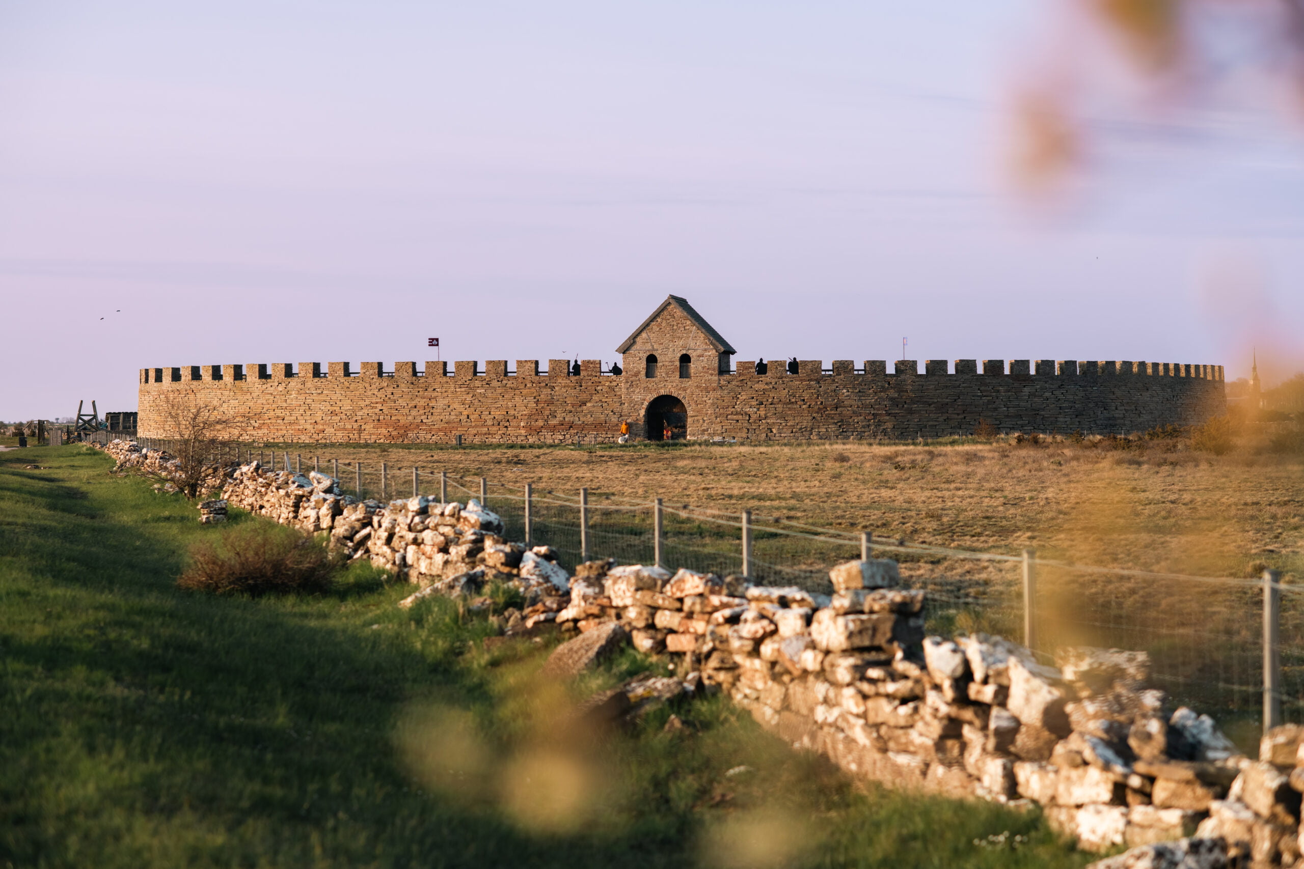 Stenmurar och ängar leder fram till en borg himlen en vårkväll med rosa himmel.